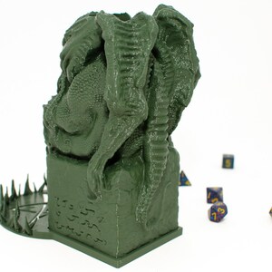 May include: Green 3D printed dragon dice tower with a circular base with spikes. The dragon is curled around a square base with runes carved into it. There are several blue and gold dice scattered around the tower.