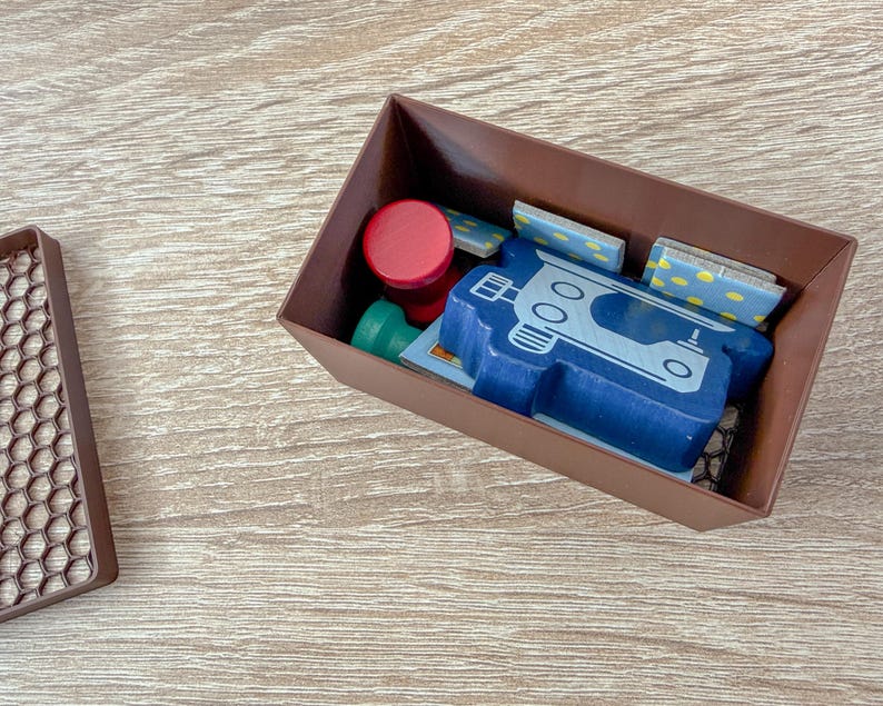 K&ouml;nnte beinhalten: Eine braune rechteckige Box enth&auml;lt verschiedene Holzspielsteine. Ein blaues, fahrzeugf&ouml;rmiges Holzteil ist prominent, zusammen mit roten und gr&uuml;nen kreisf&ouml;rmigen Teilen und kleinen rechteckigen Teilen mit gelben Punkten.