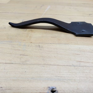 May include: Black metal door handle with a curved design and a square plate with two holes.