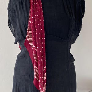 Puede incluir: Un vestido negro con una bufanda burdeos con lunares blancos. La bufanda est&aacute; drapeada sobre el maniqu&iacute;. El vestido tiene una tela texturizada y una cintura ajustada.