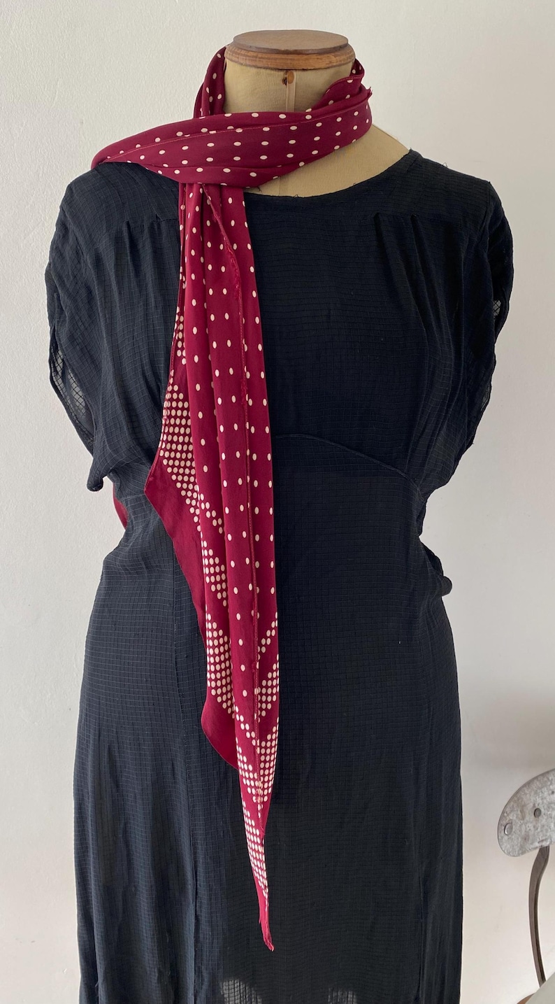 Puede incluir: Un vestido negro con una bufanda burdeos con lunares blancos. La bufanda est&aacute; drapeada sobre el maniqu&iacute;. El vestido tiene una tela texturizada y una cintura ajustada.