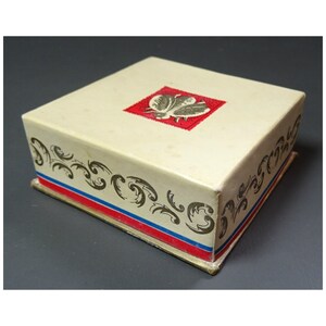 Op de afbeelding: Een witte kartonnen doos met een rode en blauwe rand. De doos heeft een gouden ontwerp aan de zijkanten en een rood vierkant met een gouden vlinderontwerp aan de bovenkant.