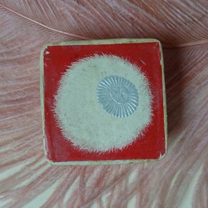 Op de afbeelding: Een rode en witte kartonnen doos met een zilveren cirkelvormig ontwerp in het midden. De doos heeft een witte cirkel met een zilveren ontwerp in het midden.