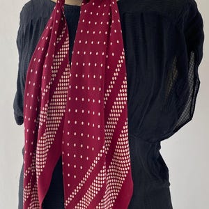 Puede incluir: Una bufanda burdeos con un estampado de lunares blancos y rayas diagonales de puntos blancos. La bufanda est&aacute; drapeada sobre una prenda negra, mostrando su dise&ntilde;o y contraste de color. La bufanda est&aacute; anudada al cuello.