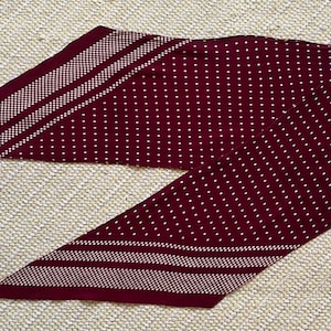 Puede incluir: Una bufanda burdeos con un estampado de lunares blancos y detalles a rayas blancas. La bufanda est&aacute; hecha de un material suave y est&aacute; doblada sobre una superficie texturizada. Este accesorio se puede usar de varias maneras.