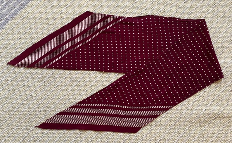 Puede incluir: Una bufanda burdeos con un estampado de lunares blancos y detalles a rayas blancas. La bufanda est&aacute; hecha de un material suave y est&aacute; doblada sobre una superficie texturizada. Este accesorio se puede usar de varias maneras.