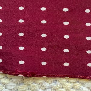 Puede incluir: Primer plano de una tela burdeos con un patr&oacute;n de lunares blancos espaciados uniformemente. La tela tiene un aspecto ligeramente texturizado y un borde cosido. Los lunares son peque&ntilde;os y circulares.