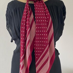 Puede incluir: Una bufanda burdeos con lunares blancos y rayas diagonales de puntos m&aacute;s peque&ntilde;os. La bufanda est&aacute; drapeada alrededor del cuello de un maniqu&iacute;, mostrando su dise&ntilde;o y textura. La bufanda est&aacute; hecha de un material suave.