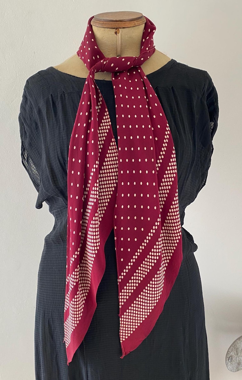 Puede incluir: Una bufanda burdeos con lunares blancos y rayas diagonales de puntos m&aacute;s peque&ntilde;os. La bufanda est&aacute; drapeada alrededor del cuello de un maniqu&iacute;, mostrando su dise&ntilde;o y textura. La bufanda est&aacute; hecha de un material suave.