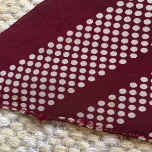 Puede incluir: Primer plano de una tela burdeos con un estampado de lunares blancos. La tela tiene un dise&ntilde;o diagonal de puntos blancos. El borde de la tela es visible, mostrando las costuras y un ligero deshilachado.