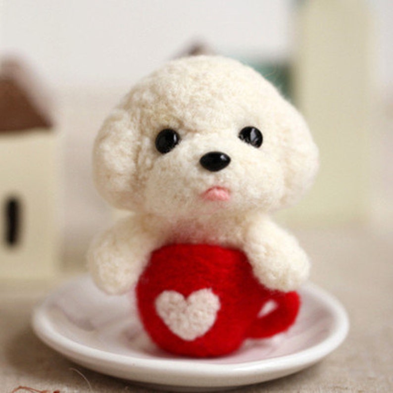 May include: A white felt poodle holding a red felt cup with a white heart on it. The cup is sitting on a white saucer.