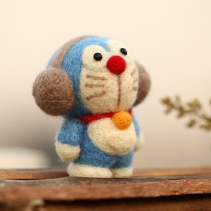 May include: A blue and brown felt toy with a red nose and a yellow collar. The toy has large ears and a friendly expression.