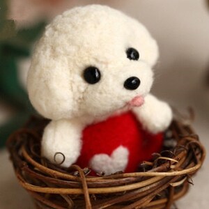 May include: White felt dog toy wearing a red felt dress with a white heart. The dog is sitting in a woven brown nest.