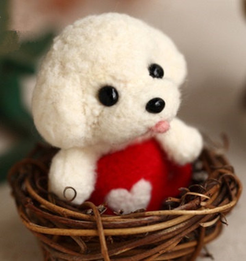 May include: White felt dog toy wearing a red felt dress with a white heart. The dog is sitting in a woven brown nest.