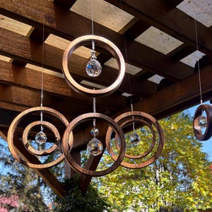 May include: A wooden mobile with five circular rings and crystal prisms hanging from the rings. The mobile is hanging from a wooden ceiling.