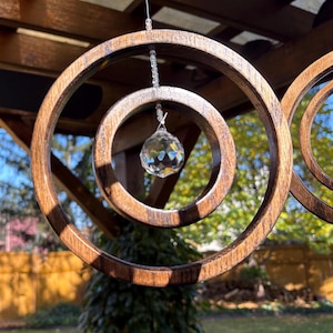 May include: A wooden hanging mobile with three concentric circles, the largest of which is stained a dark brown. A crystal prism hangs from the center of the mobile.