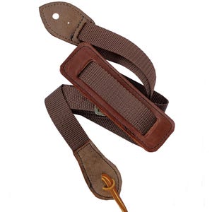 May include: A brown guitar strap with a leather shoulder pad and suede ends. The strap is made of woven nylon and has a metal buckle. The strap is approximately 5 cm wide.