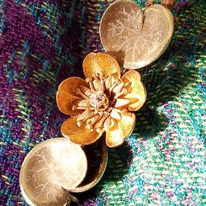 May include: A gold-toned brooch featuring a stylized flower with a single diamond in the center, surrounded by two leaves.