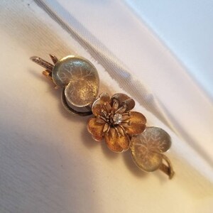 May include: A gold and silver brooch featuring a stylized flower with a single diamond in the center, surrounded by two leaves.