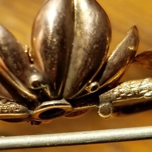 May include: Gold-toned brooch with a floral design. The brooch has a pin and catch closure on the back.