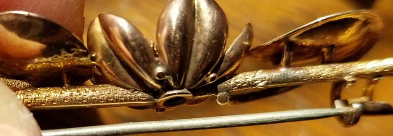May include: Gold-toned brooch with a floral design. The brooch has a pin and catch closure on the back.