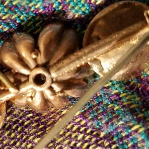 May include: Gold tone flower brooch with a pin on the back. The flower has a textured surface and a small round center.