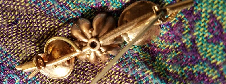 May include: Gold tone flower brooch with a pin on the back. The flower has a textured surface and a small round center.