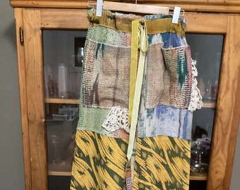 Op de afbeelding: Gele, groene, blauwe en bruine patchwork broek met witte kant. De broek heeft een gele lint strik.