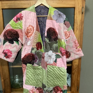 May include: A pink and green patchwork jacket with floral print. The jacket has a long, open front and a quilted design.