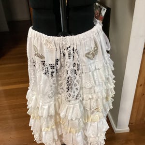 May include: A white lace skirt with multiple layers of frills. The skirt has two silver butterfly embellishments on the front.