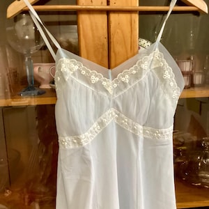 May include: A light blue, sheer, sleeveless slip with white lace trim. The slip has a V-neckline and a flowy skirt.