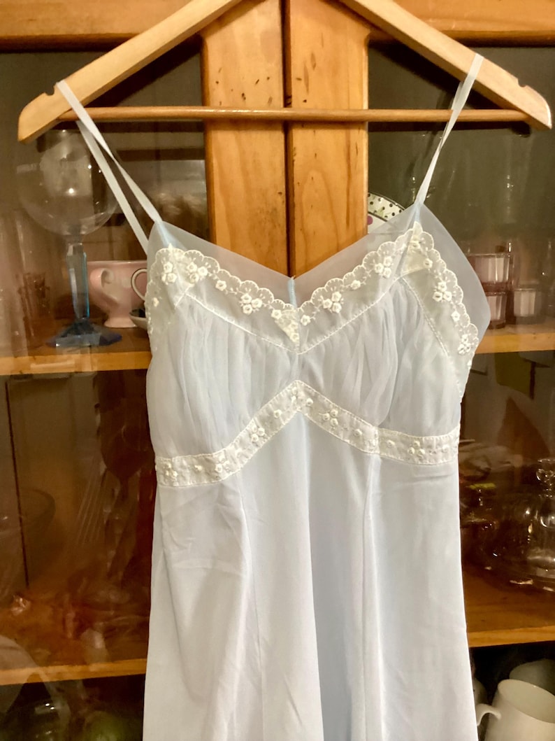 May include: A light blue, sheer, sleeveless slip with white lace trim. The slip has a V-neckline and a flowy skirt.