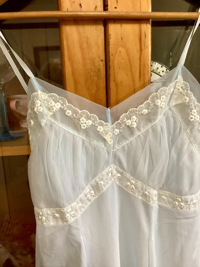 May include: A light blue sheer slip with white lace trim. The lace trim features a delicate floral pattern.