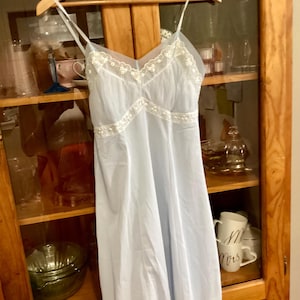 May include: A light blue slip dress with white lace trim. The dress has a V-neckline and spaghetti straps.