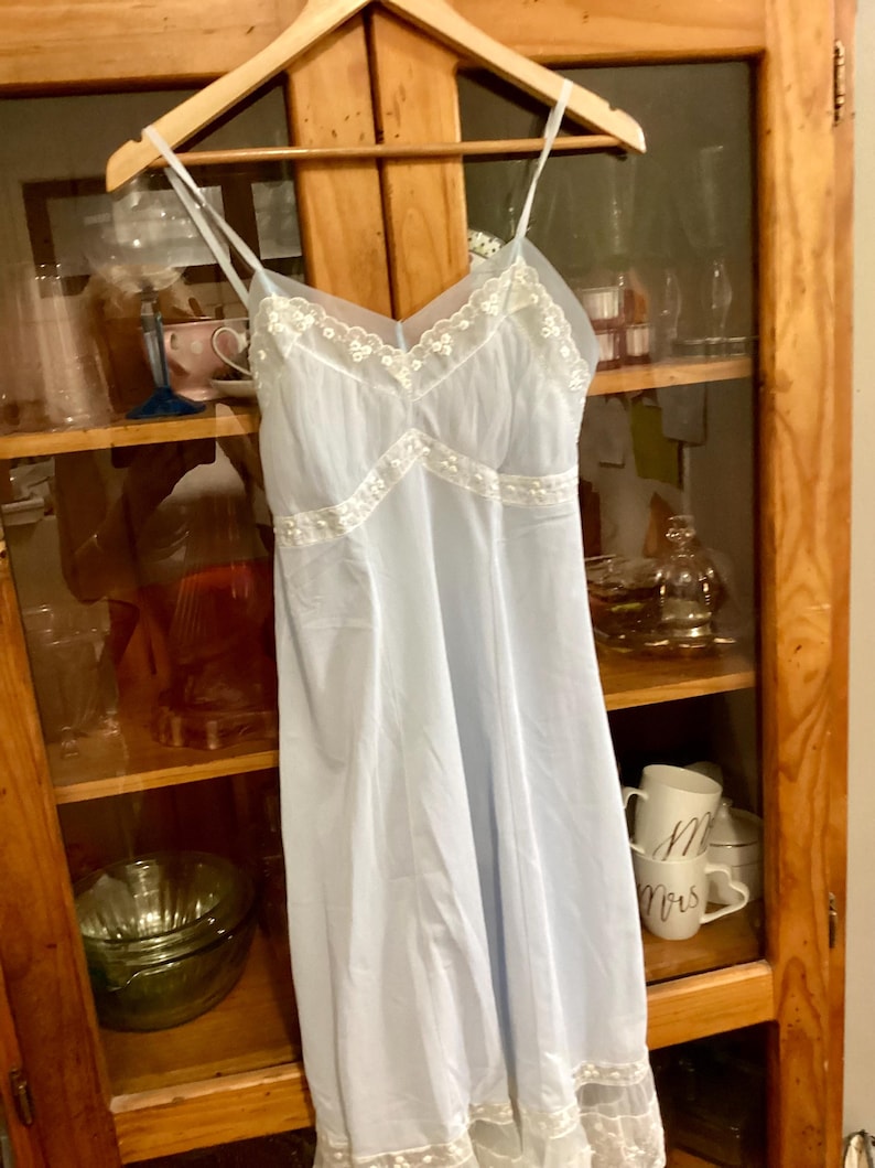 May include: A light blue slip dress with white lace trim. The dress has a V-neckline and spaghetti straps.