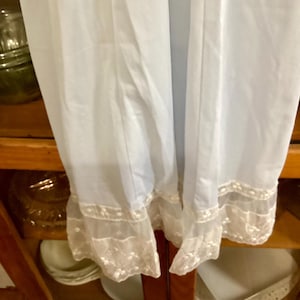 May include: White slip with a lace trim. The slip is made of a sheer fabric and has a delicate lace trim around the bottom.