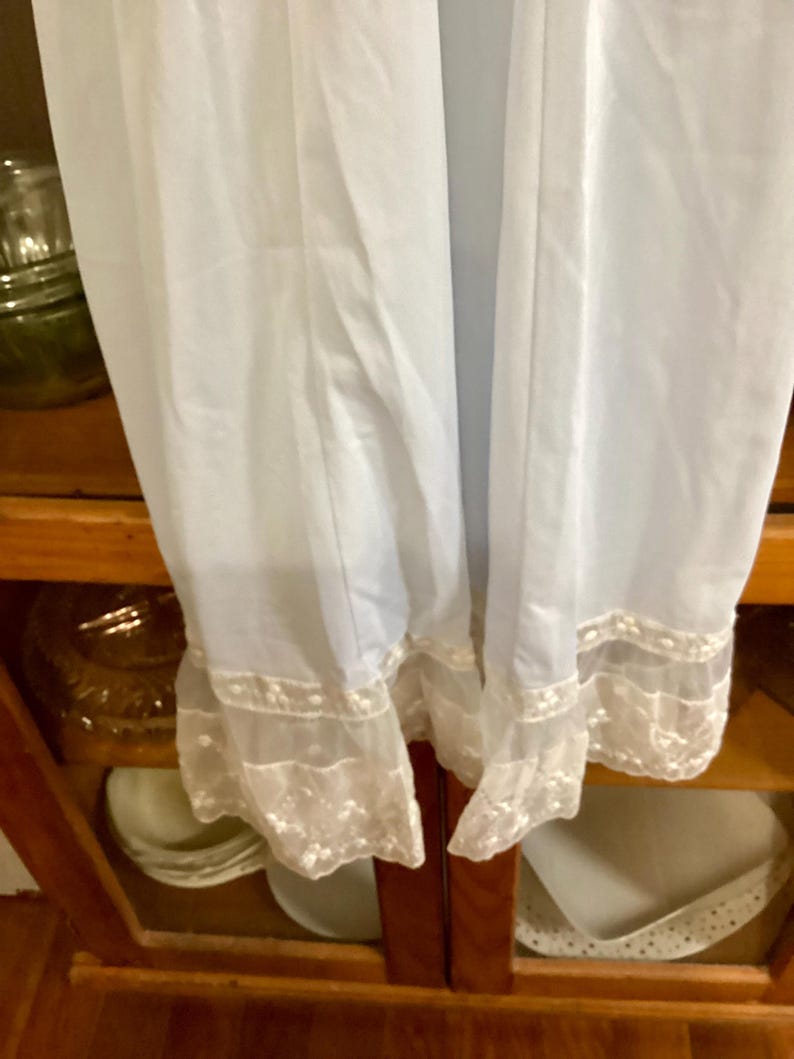 May include: White slip with a lace trim. The slip is made of a sheer fabric and has a delicate lace trim around the bottom.