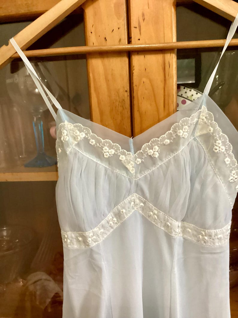 May include: A light blue, sheer slip with white lace trim. The lace trim features a delicate floral pattern.