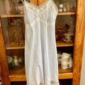 May include: A light blue slip dress with white lace trim. The dress has a delicate floral pattern and a scalloped hem.