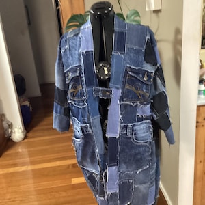 May include: A long denim jacket made from patchwork denim fabric. The jacket has a long, flowing silhouette and features a variety of different denim washes and textures.