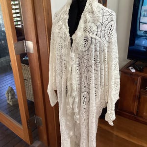 May include: A white crocheted lace shawl with a scalloped edge and intricate floral patterns.