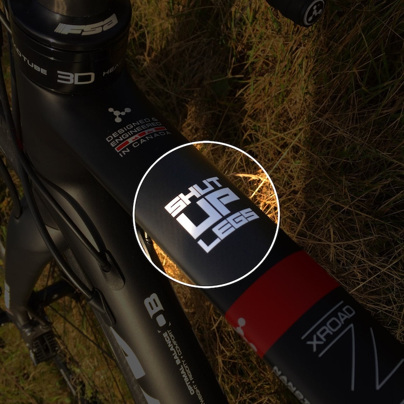 Puede incluir: Marco de bicicleta negro con una pegatina blanca que dice "SHUT UP LEGS" y una franja roja con la palabra "XROAD" en ella.