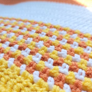 May include: Close-up of a crocheted blanket with stripes of yellow, orange, and white yarn.