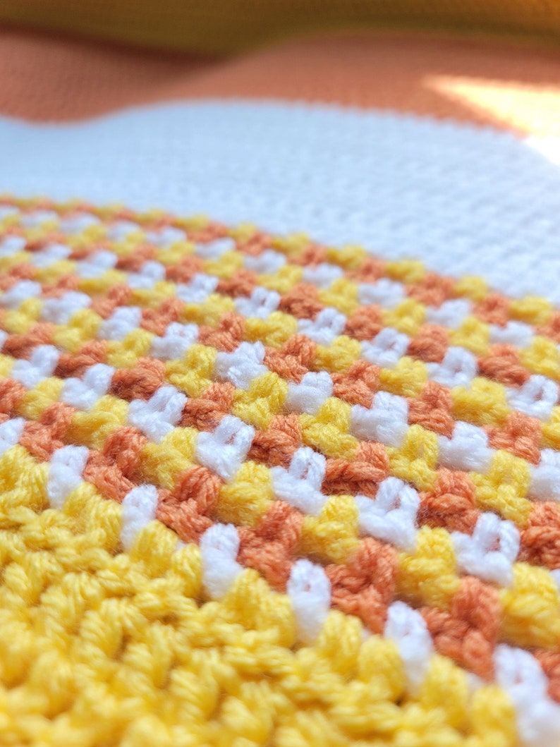 May include: Close-up of a crocheted blanket with stripes of yellow, orange, and white yarn.