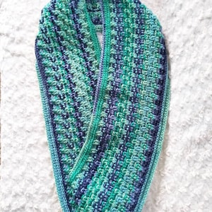 May include: A crocheted infinity scarf in shades of blue and green. The scarf is made with a textured stitch and has a fringed edge.