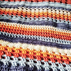 May include: A crocheted blanket with stripes of blue, orange, red, and white yarn.