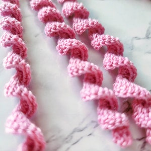 May include: Three strands of pink crocheted yarn twisted into a spiral shape.