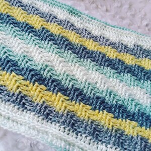 May include: A crocheted baby blanket with a chevron pattern in shades of blue, green, white, and yellow.