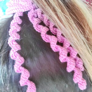 May include: Pink crocheted hair tie with a spiral design. The hair tie is made of soft yarn and is perfect for adding a touch of color to any hairstyle.
