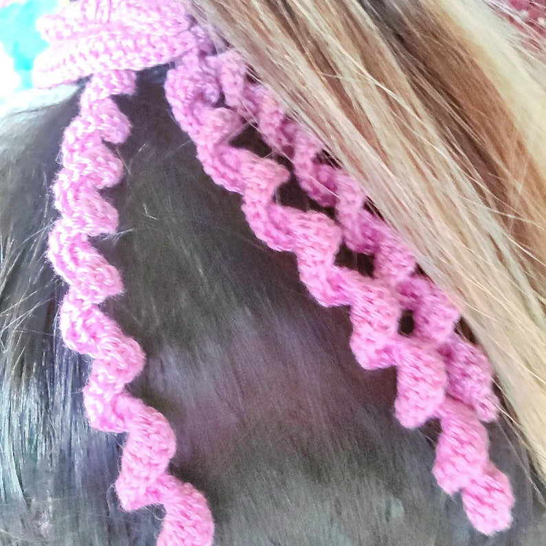 May include: Pink crocheted hair tie with a spiral design. The hair tie is made of soft yarn and is perfect for adding a touch of color to any hairstyle.